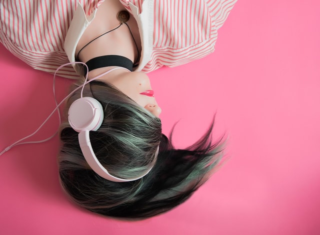 Woman wearing headphones with a pink background - Photo by Elice Moore on Unsplash